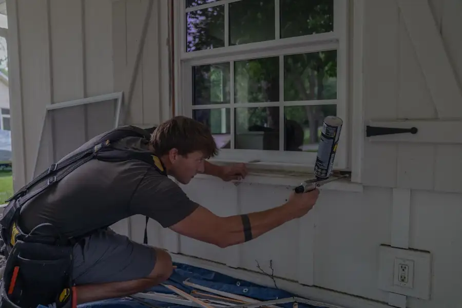 A Window Guys installer sealing the exterior of a new window