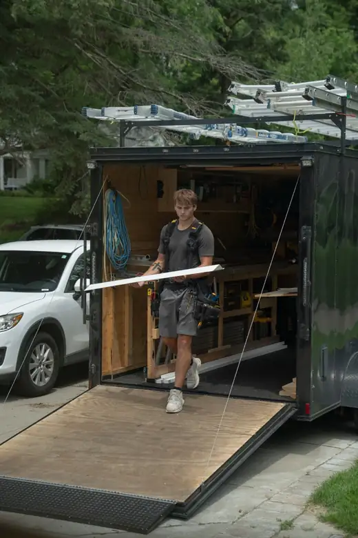 A Window Guys crew member carrying a piece of custom-bent flashing from the work trailer